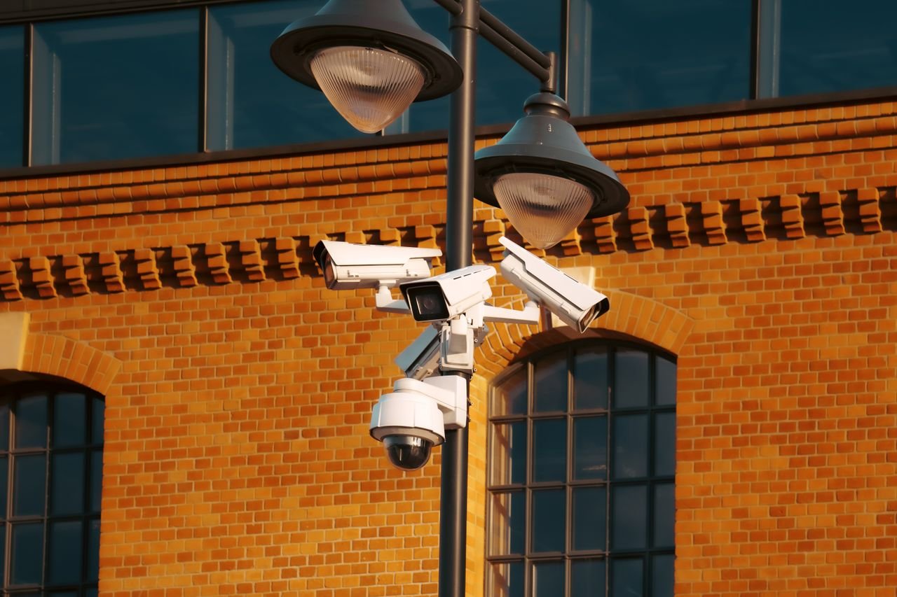Home Modern security cameras mounted on a pole against a brick building in the city.