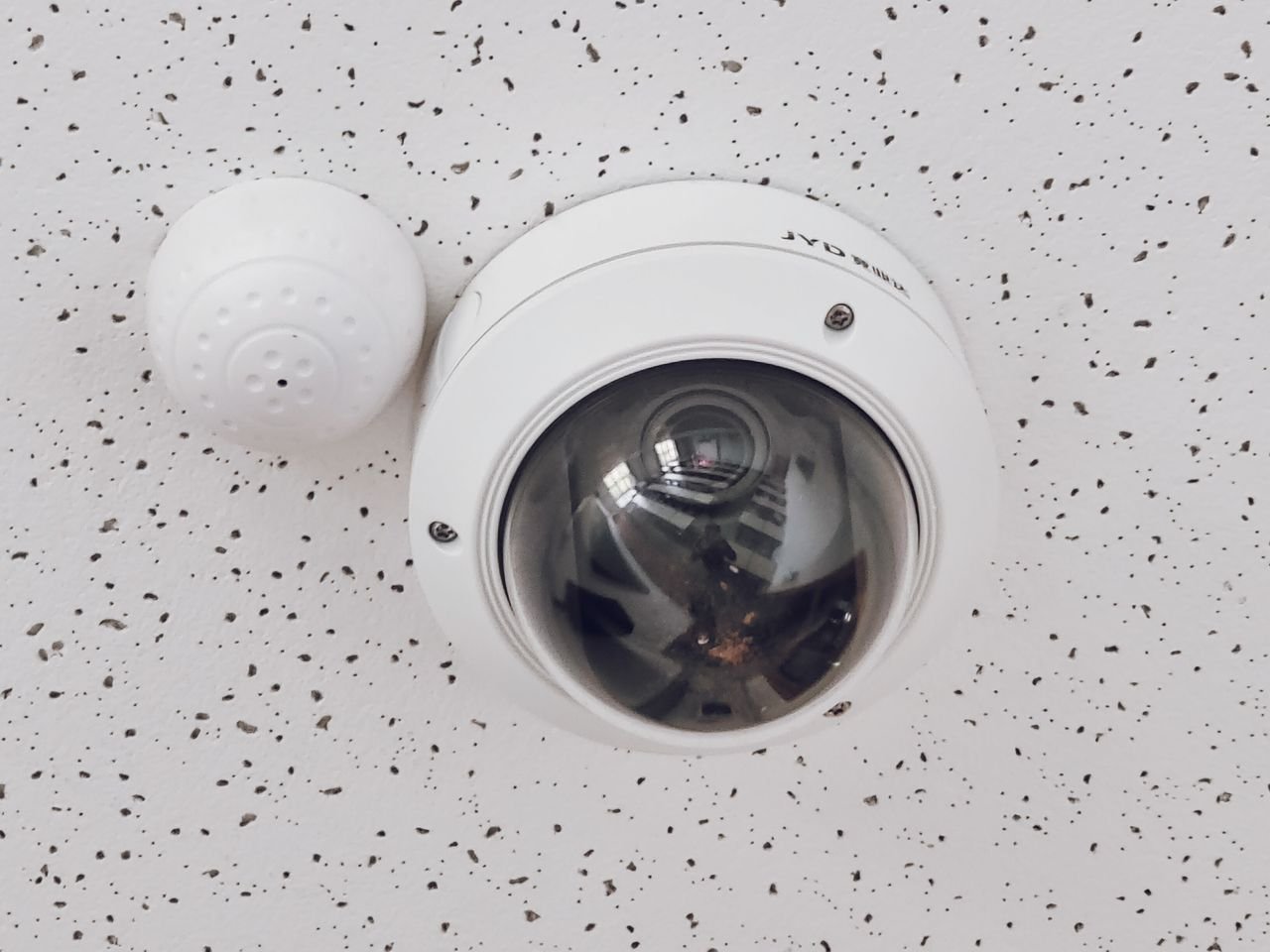 Home Close-up of a round dome surveillance camera installed on a speckled ceiling for security monitoring.